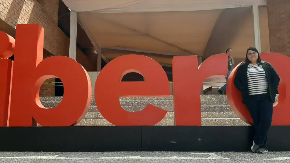 Colour photo of Mireia Vidal i Quintero stood in front of a sign outside of a building. The sign reads "ibero".