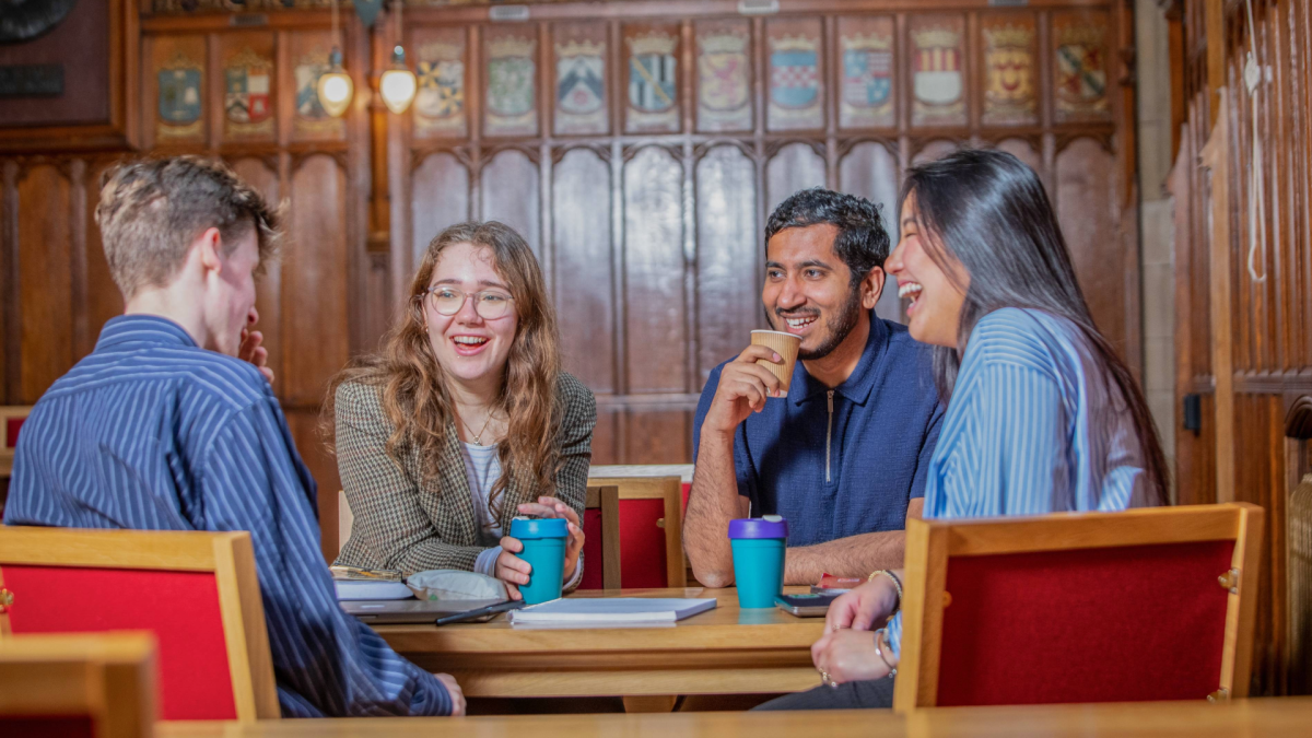 Colour photo of four students sat at a table in the Rainy Hall, laughing and smiling as they chat with one another