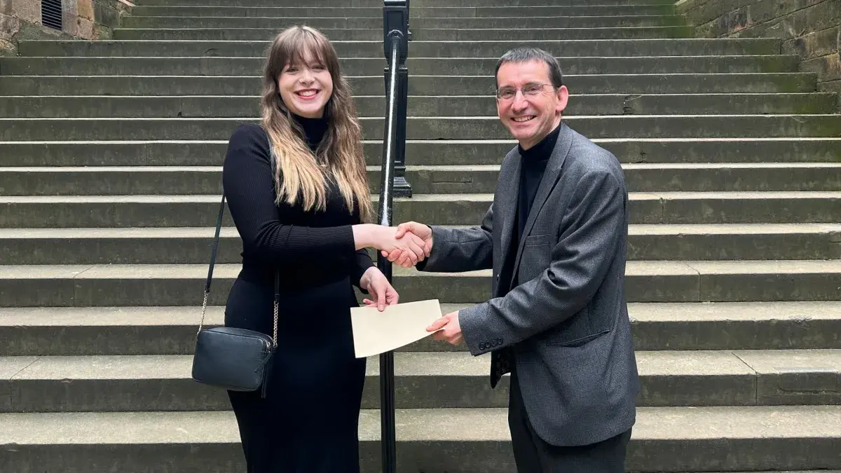 Colour photo of Professor Jeremy Carrette shaking hands with competition winner Farrah Hughes as he passes her an envelope