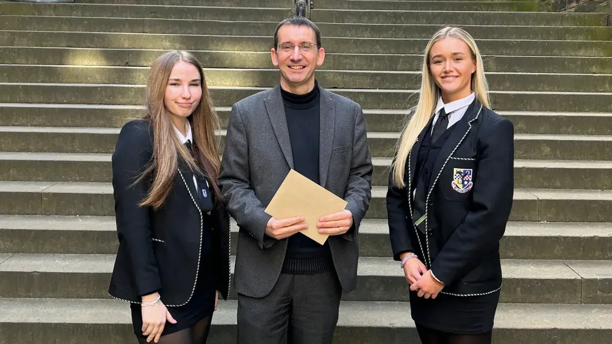 Colour photo of Professor Jeremy Carrette stood holding an envelope beside competition prize winners Kirsty Alston and Holly Bryce 