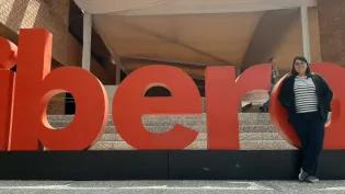 Colour photo of Mireia Vidal i Quintero stood in front of a sign outside of a building. The sign reads "ibero".