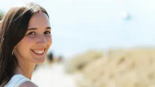 Colour head and shoulders photo of Sophie stood looking back at the camera and smiling