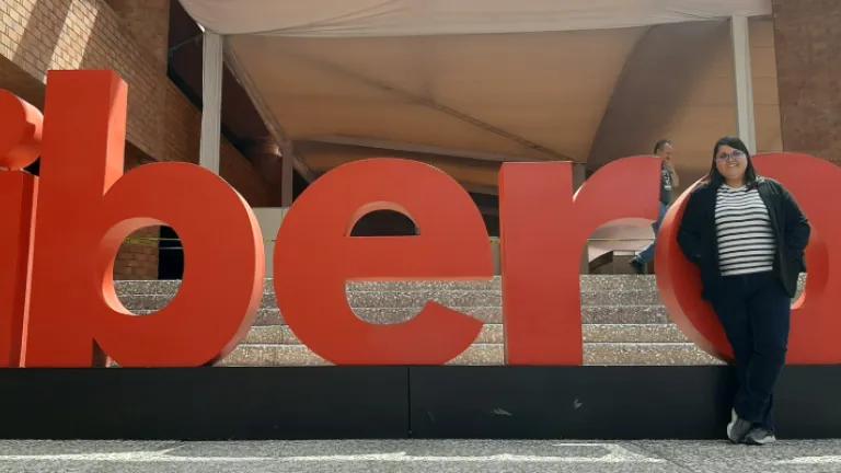Colour photo of Mireia Vidal i Quintero stood in front of a sign outside of a building. The sign reads "ibero".