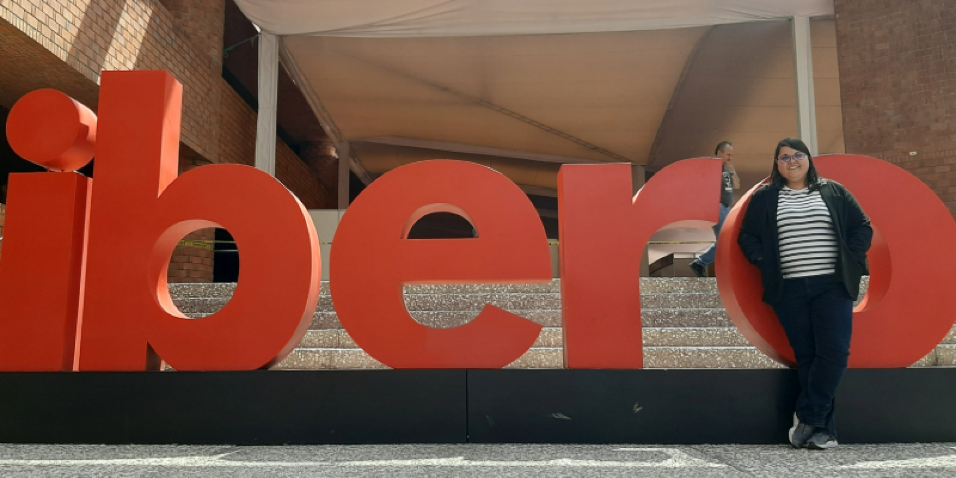 Colour photo of Mireia Vidal i Quintero stood in front of a sign outside of a building. The sign reads "ibero".