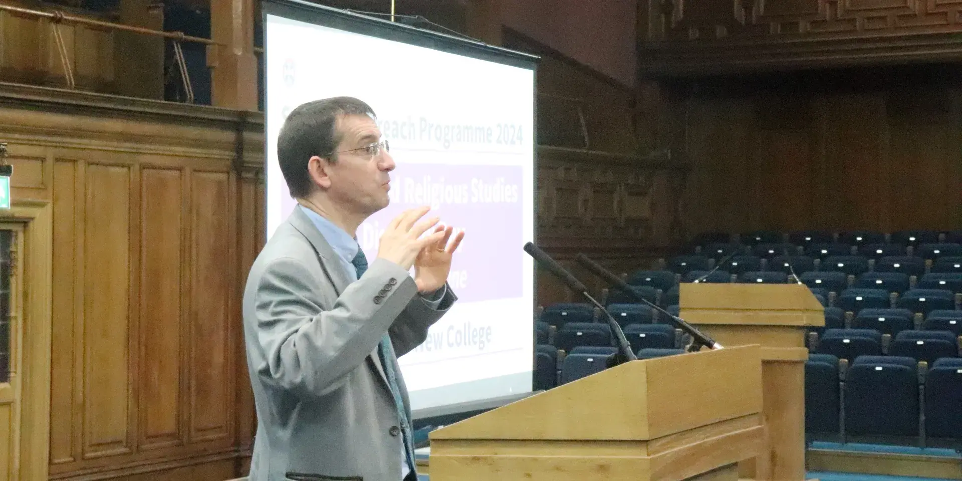 Colour photo of Professor Jeremy Carrette speaking at a lectern in the Assembly Hall