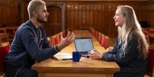 Colour photo of two School of Divinity students sat talking at a table in Rainy Hall