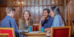 Colour photo of four students sat at a table in the Rainy Hall, laughing and smiling as they chat with one another