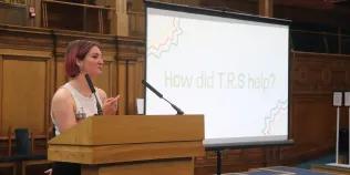 Colour photo of a Beth Jones speaking at a lectern in the Assembly Hall