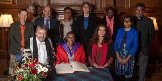 Colour photo of Esther Mombo receiving her honorary doctorate whilst sat at a table with other members of the University of Edinburgh. Everyone is smiling at the camera.
