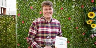 Colour head and shoulders photo of Stephen Dolan stood holding his Student Teacher of the Year trophy and certificate