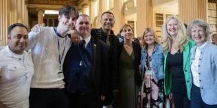 Colour photo of School of Divinity staff members stood together smiling at the camera in Playfair Library