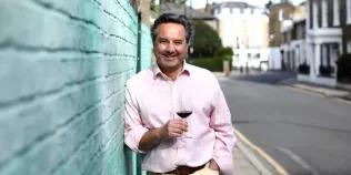 Colour head and shoulders photo of Will Lyons smiling whilst holding a wine glass