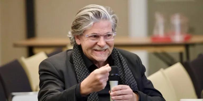 Colour photo of Jan-Werner Müller sat in the Martin Hall speaking a microphone that he is holding