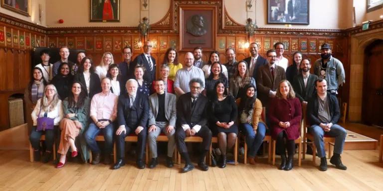 Colour photo of School of Divinity staff and students seated and standing in the Rainy Hall with Cornel West as they all smile at the camera