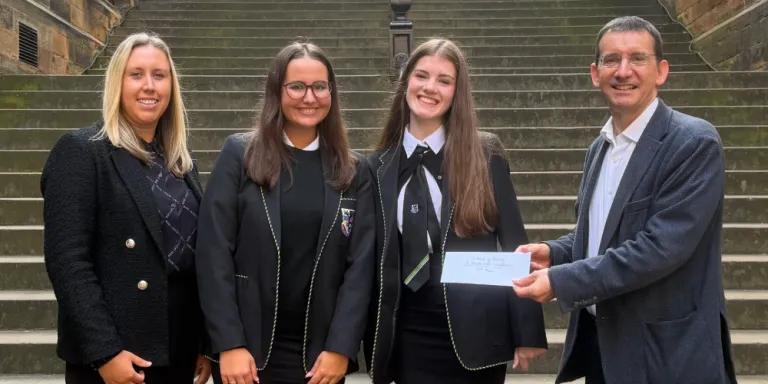 Colour photo of (Left to right) Gillian, Hannah, Jessica and Professor Jeremy Carrette stood in the New College Quad smiling at the camera. Professor Jeremy Carrette is holding a prize voucher