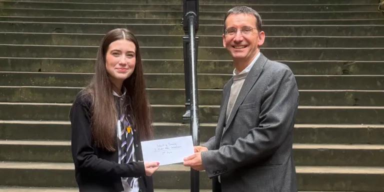 Colour photo of (Left to right) Anna and Professor Jeremy Carrette stood in the New College Quad smiling at the camera. Professor Jeremy Carrette is holding a prize voucher with Anna