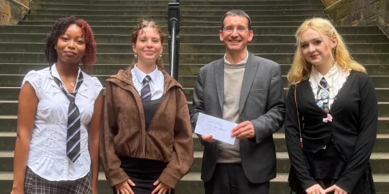 Colour photo of (Left to right) Miral, Alice, Professor Jeremy Carrette and Halle stood in the New College Quad smiling at the camera. Professor Jeremy Carrette is holding a prize voucher