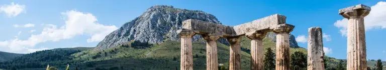 Colour photo of stone pillars in front of a hill landscape. ©Davide Mauro, Pixabay, https://commons.wikimedia.org/wiki/File:Tempio_di_Apollo_e_Acrocorinto.jpg 