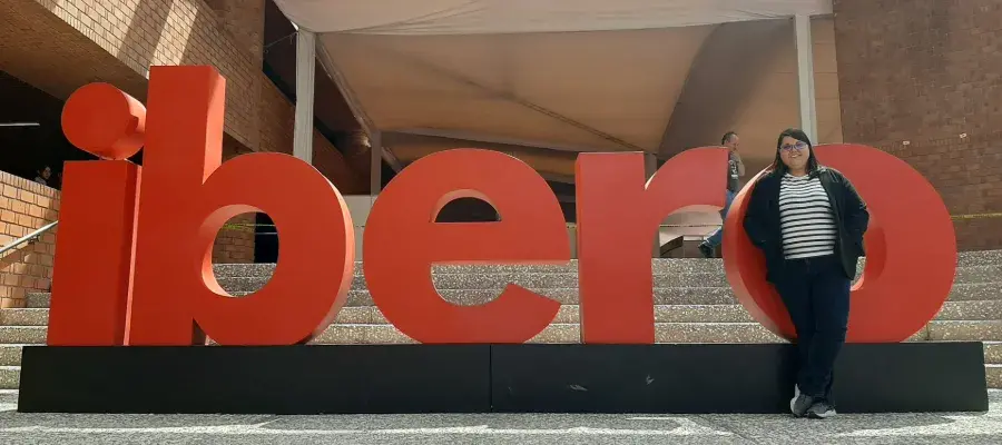 Colour photo of Mireia Vidal i Quintero stood in front of a sign outside of a building. The sign reads "ibero".