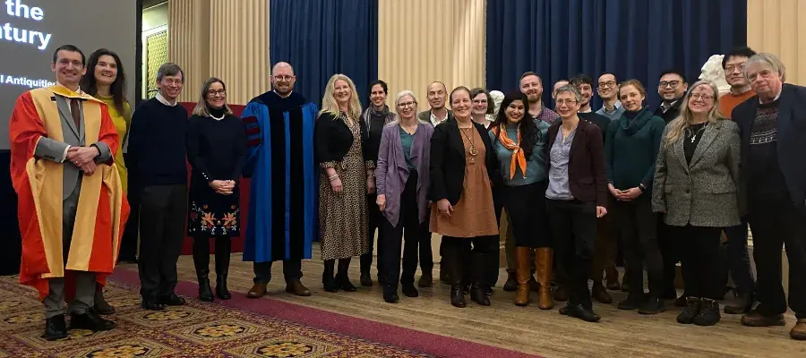 Colour head and shoulders photo of School of Divinity academic staff members stood together smiling at the camera in the Playfair Library