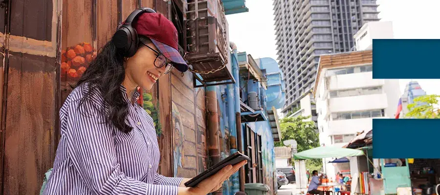 Colour photo of a student smiling looking at a tablet whilst they sit in the street of a city