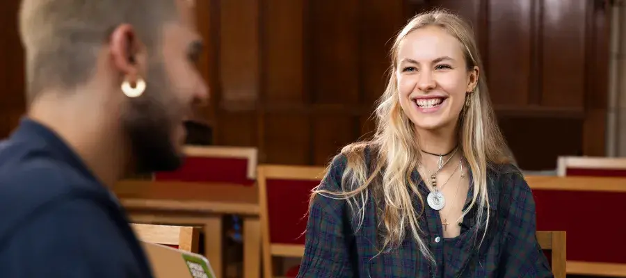 Colour photo of a student smiling whilst sat across the table at another student in the Rainy Hall