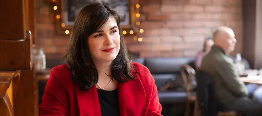 Colour photo of a student thinking and smiling as they look off into the distance while sat in a cafe