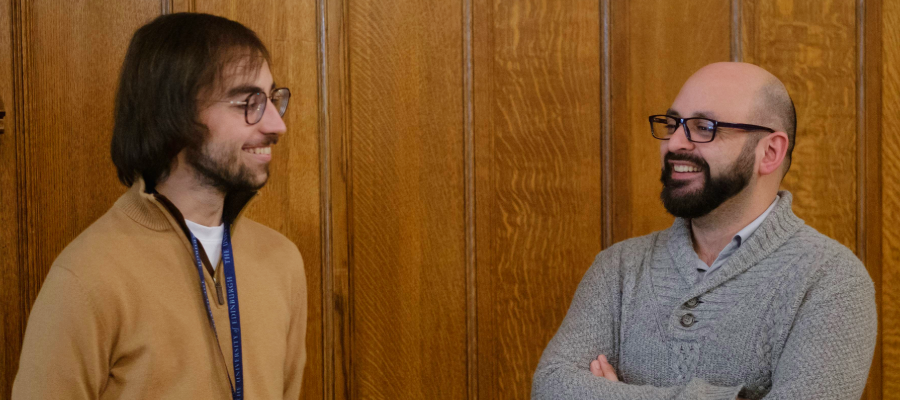 Colour photo of two students stood smiling and talking to one another in the Rainy Hall
