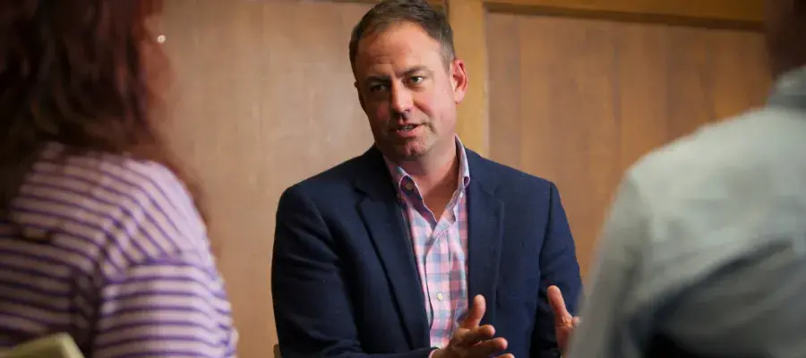 Colour photo of Dr Joshua Ralston speaking to a student whilst both are sat in the Martin Hall
