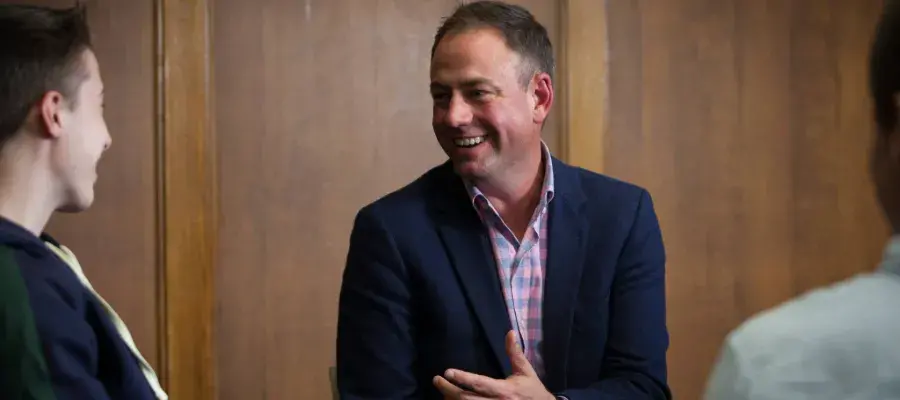 Colour photo of Dr Joshua Ralston smiling whilst speaking to a student whilst both are sat in the Martin Hall