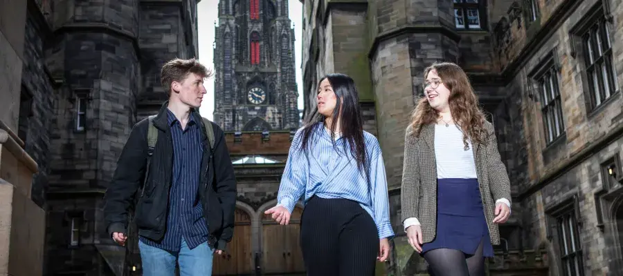 Colour photo of three students walking together and speaking in the New College Quad