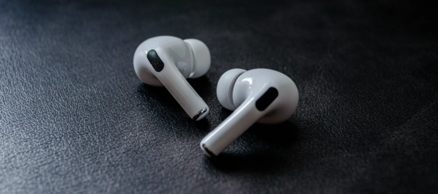 Colour photo of a pair of Airpods lying on a black surface