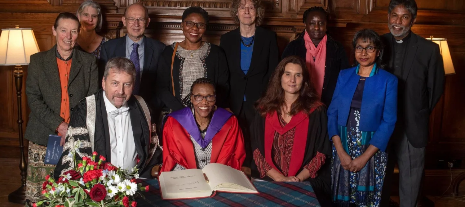 Colour photo of Esther Mombo receiving her honorary doctorate whilst sat at a table with other members of the University of Edinburgh. Everyone is smiling at the camera.