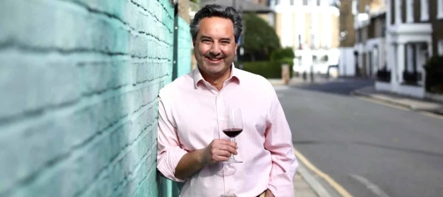 Colour head and shoulders photo of Will Lyons smiling whilst holding a wine glass