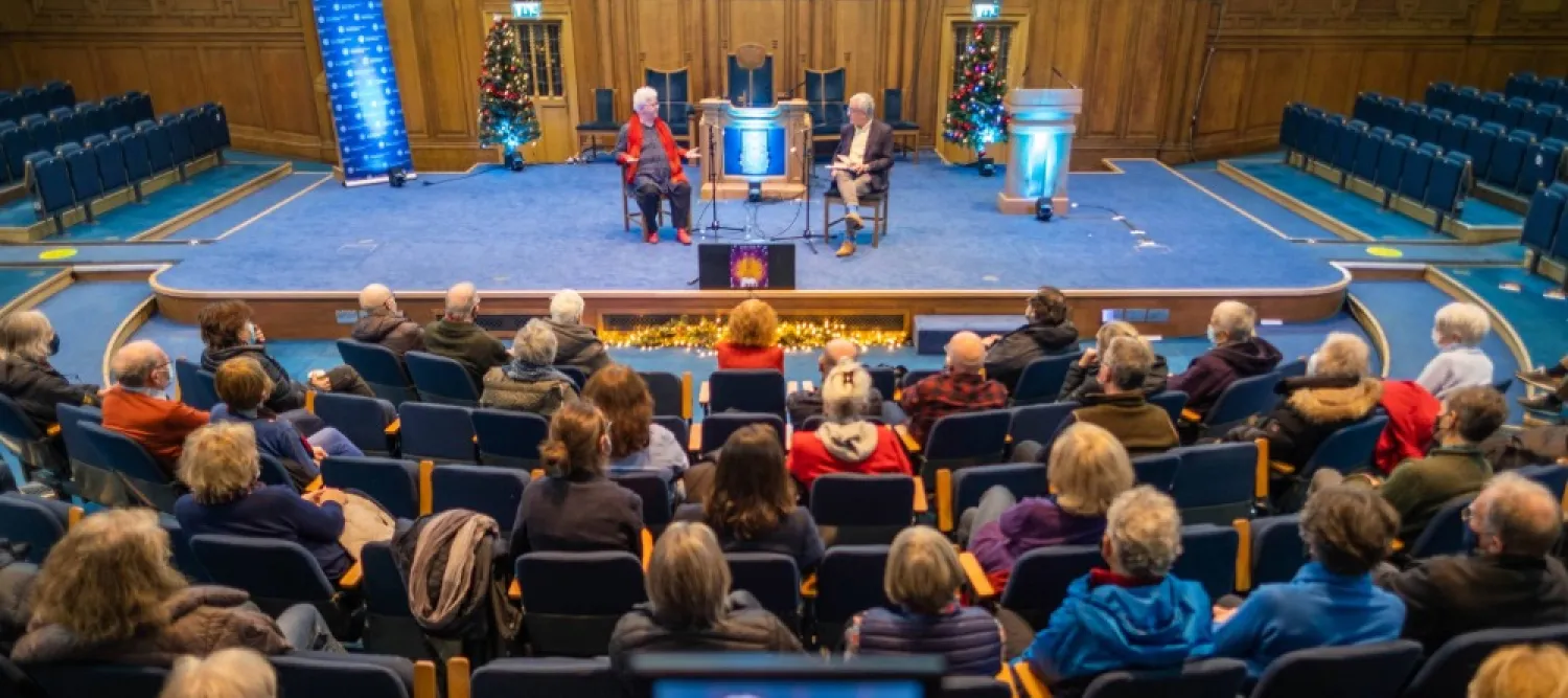 Colour photo of people sat in the Assembly Hall watching two people speak whilst sat on the stage