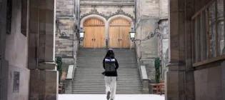 Colour photo of a student walking through the archway into the New College Quad. They are walking away from the camera with their back facing the viewer.