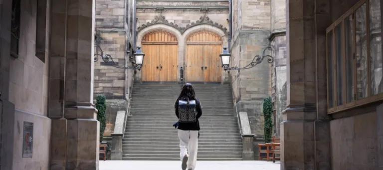 Colour photo of a student walking through the archway into the New College Quad. They are walking away from the camera with their back facing the viewer.