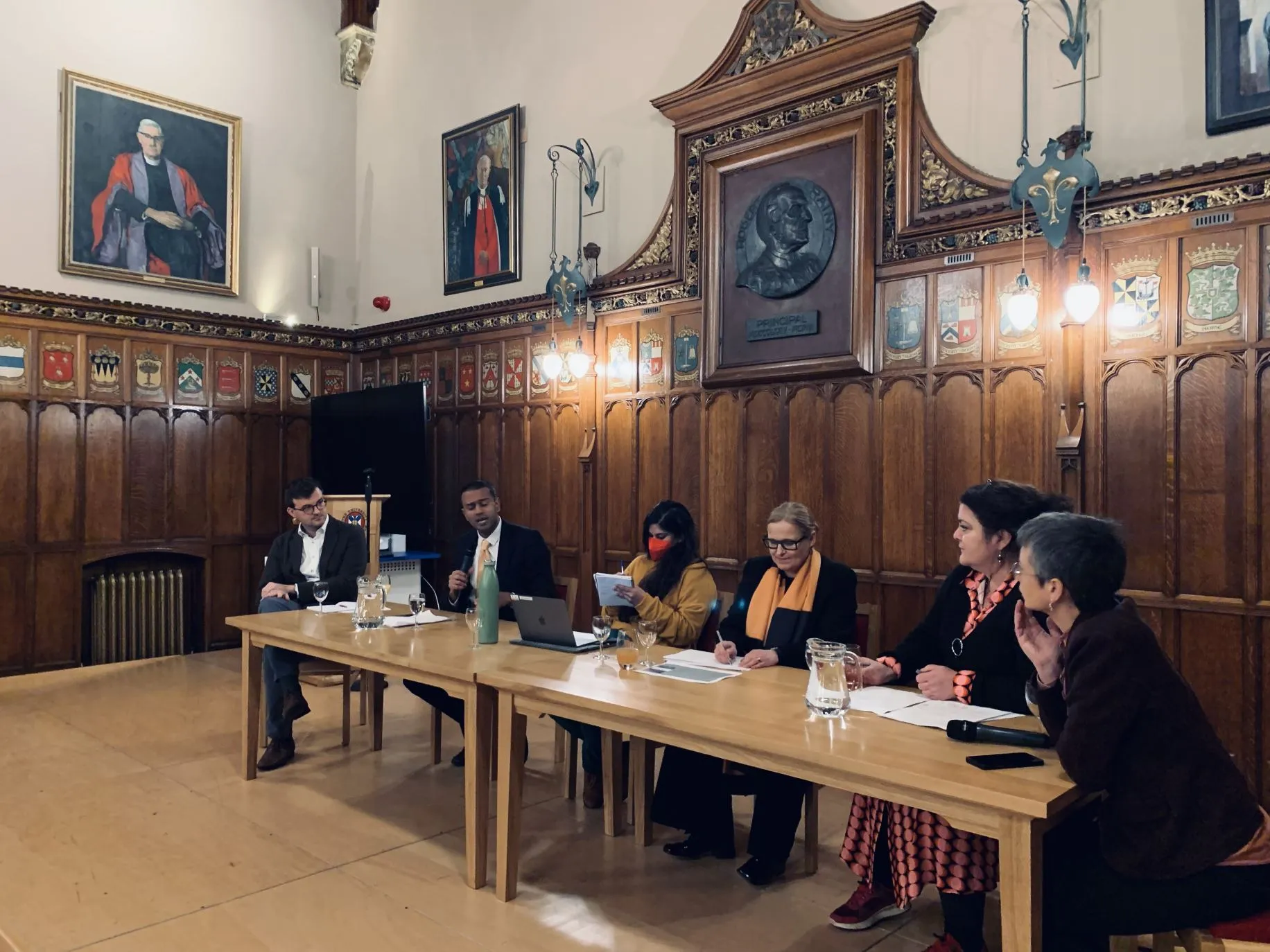 Coloured photo of a panel of speakers in Rainy Hall