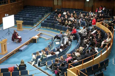 Colour birds eye photo of School Pupils sat in the Assembly Hall listening to Dr Upali Sraman speak as he sits on the stage in the hall