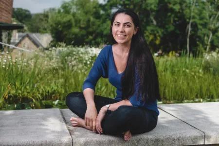 Colour photo of Francesca Stavrakopoulou sat cross legged whilst smiling at the camera