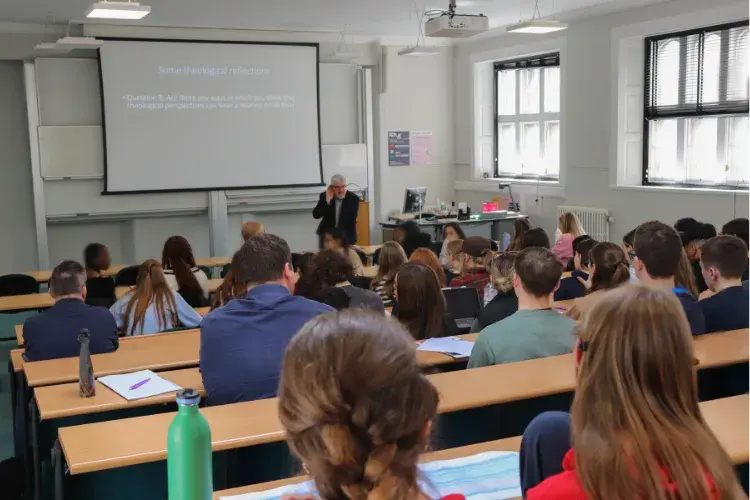 Dr Michael Fuller presents a powerpoint presentation to students in a large lecture theatre with tiered seating
