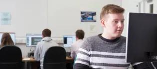 Colour head and shoulders photo of Marc Livingstone sat in a computer lab looking at a computer screen