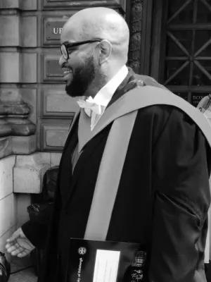 Black and white photo of Eric Lewis in his graduation gown. The photo is taken from the side as Eric faces to the left of the photo
