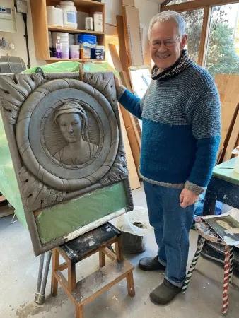 Colour photo of Tim Chalk stood smiling at the camera with the in-progress Mary of Guise plaque beside him